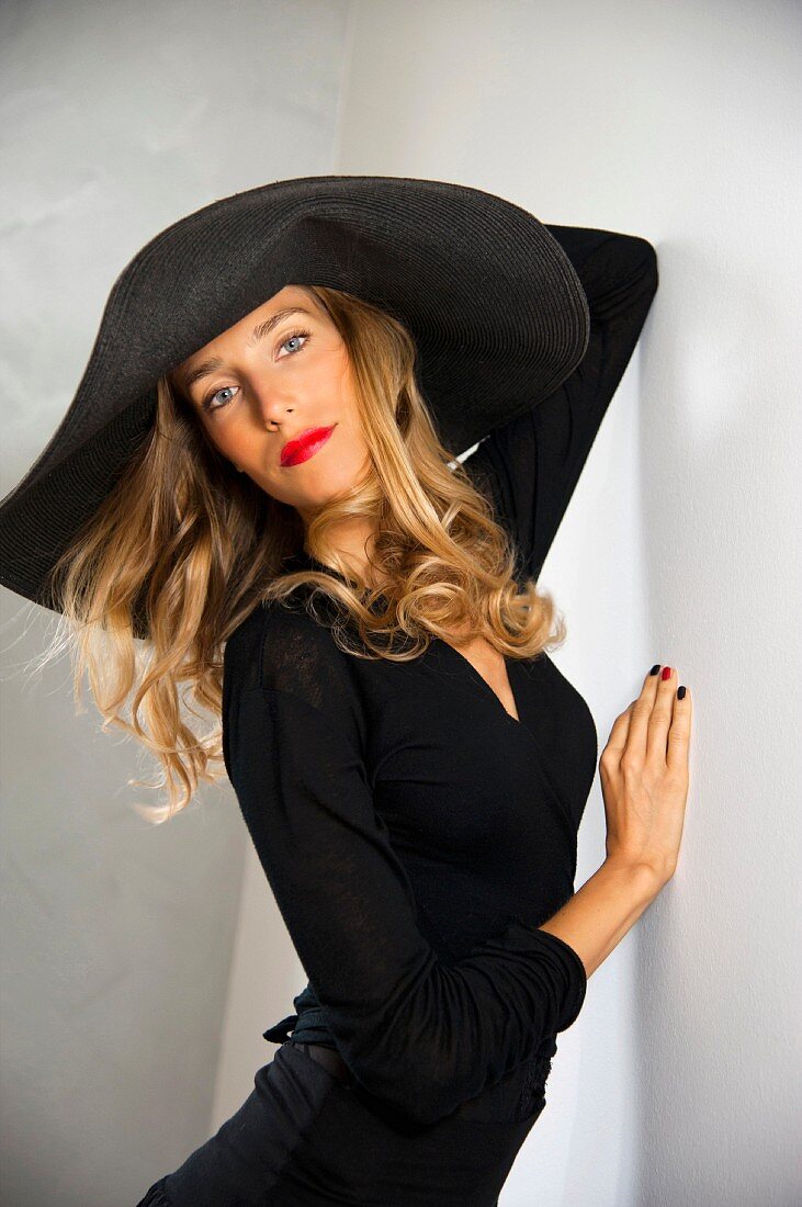 A blonde woman wearing a black dress with a big hat