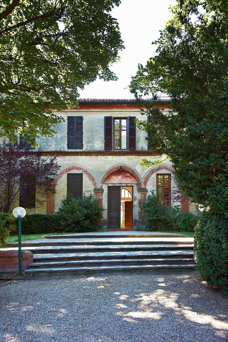 Kiesweg und breite Stufen zu historischem, italienischen Landhaus mit Ziegelbögen und Fensterläden
