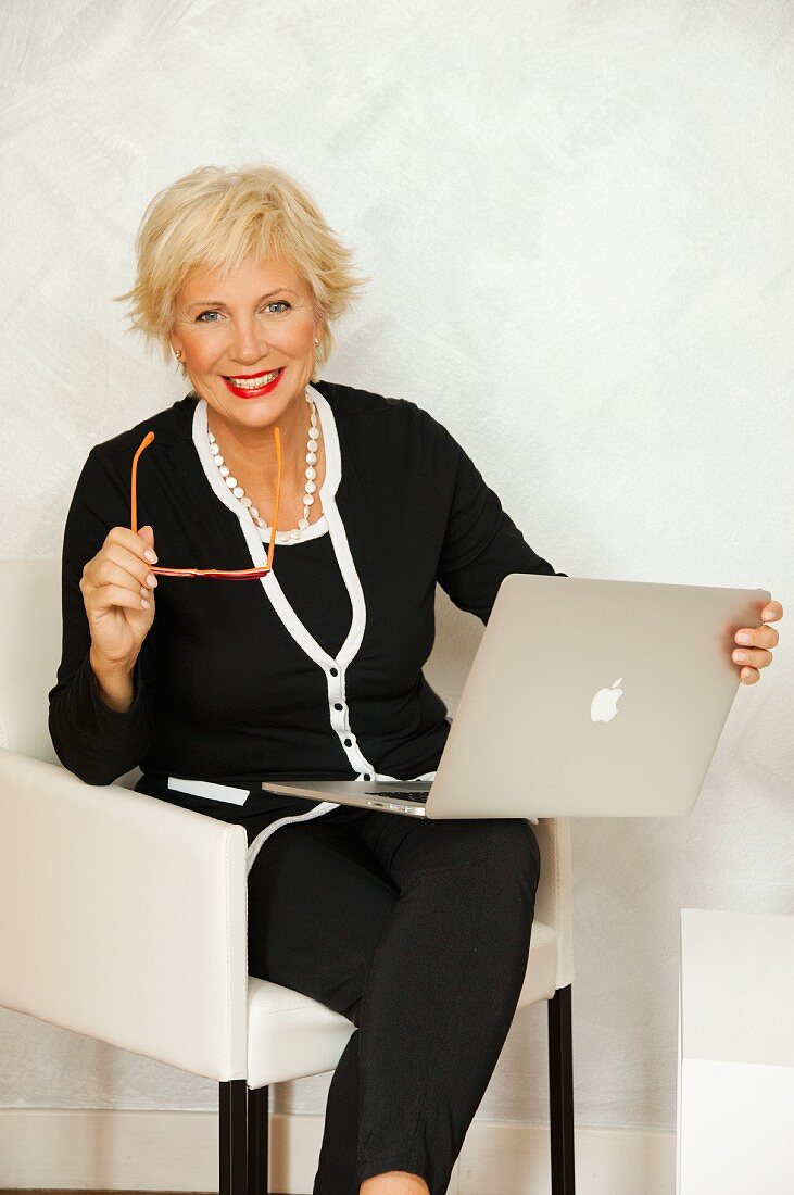 An older business woman sitting in an armchair with a laptop