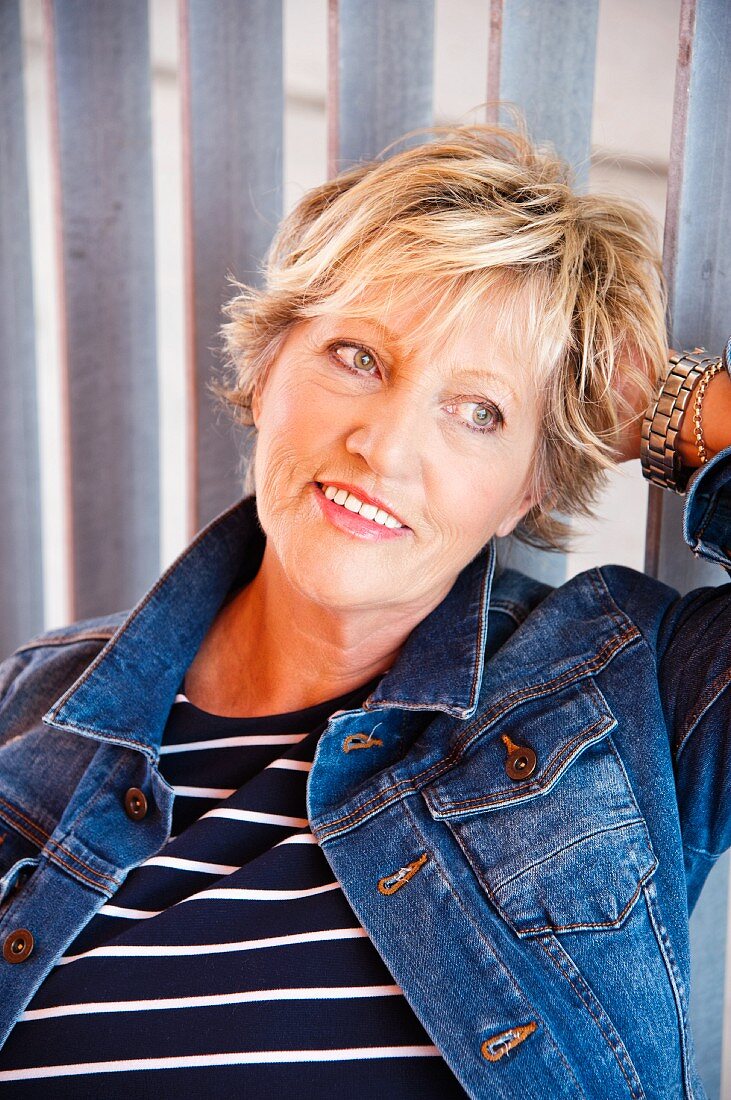 A portrait of an older woman in a denim jacket and a stripped shirt