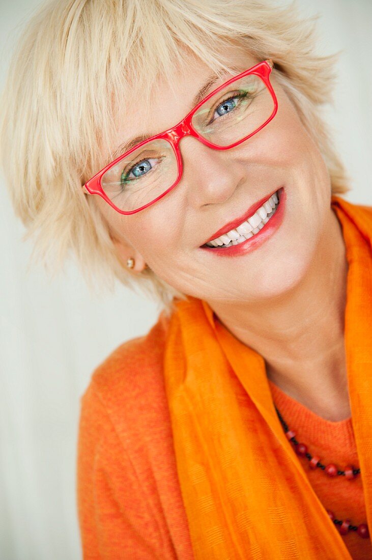 An older woman wearing an orange jumper and scarf and a pair of red glasses