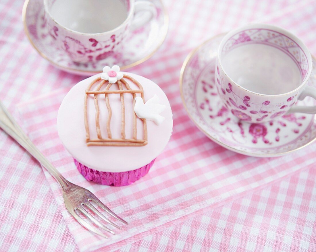 A cupcake decorated with a dove and a cage