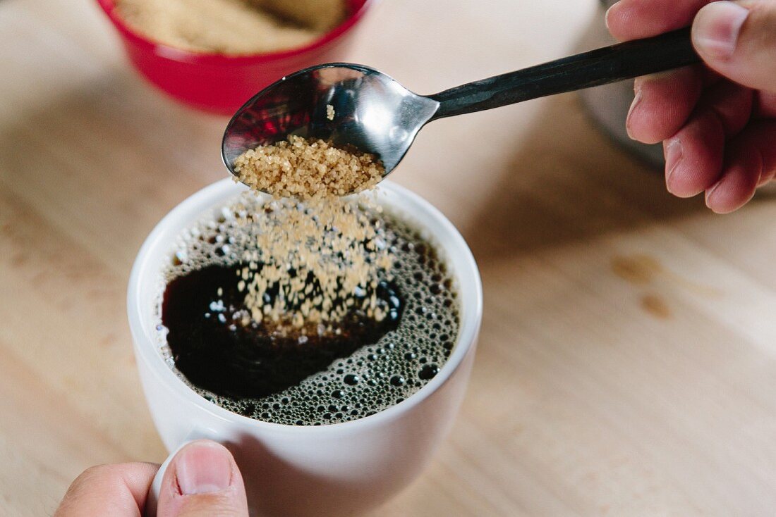 Brown sugar being sprinkled into a cup of coffee