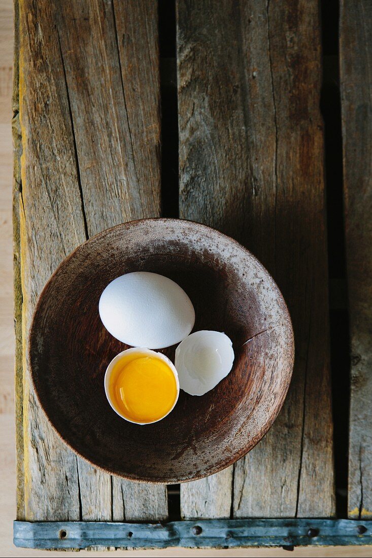 Ganzes und zerbrochenes Ei in Holzschale (Draufsicht)