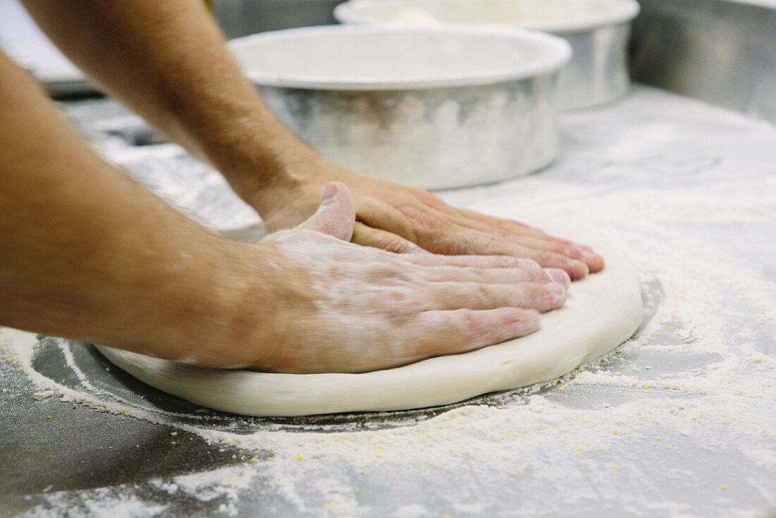 Pizzabäcker drückt Teig flach