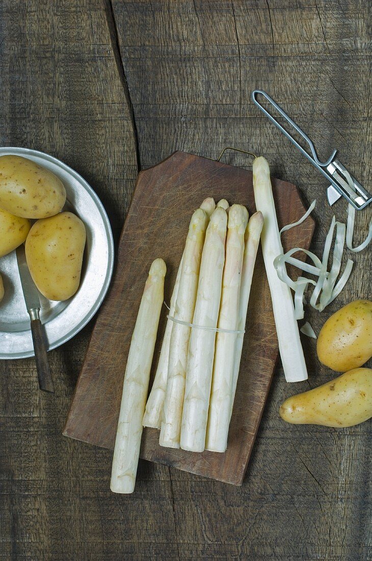 Frischer weisser Spargel mit Spargelschäler daneben neue Kartoffeln