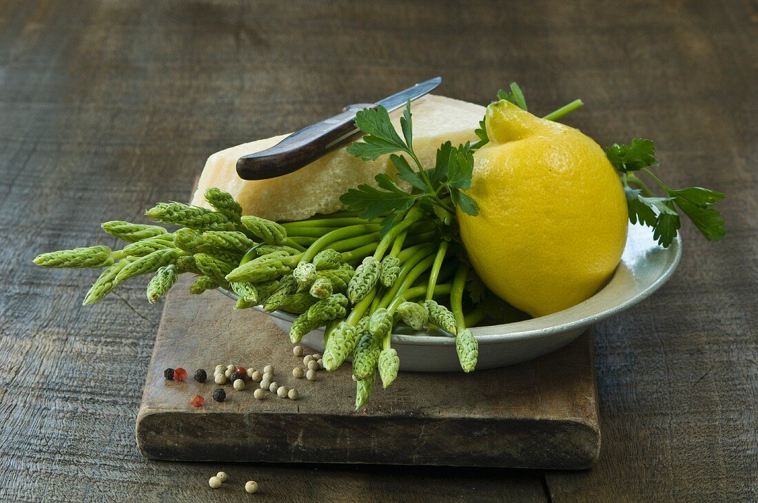 Wild asparagus, a lemon, Parmesan cheese and parsley in a bowl on a wooden board