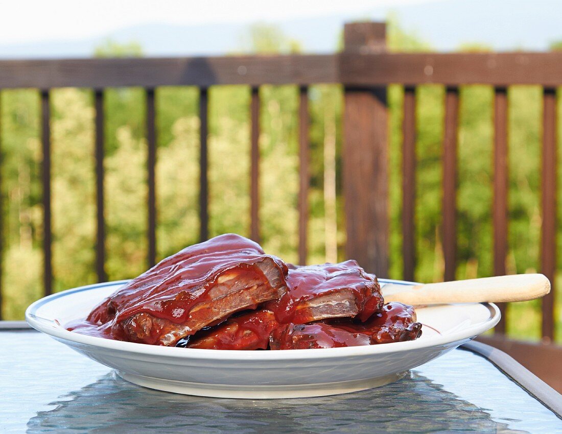 Raw beef ribs for grilling being marinated in barbecue sauce on a table outside