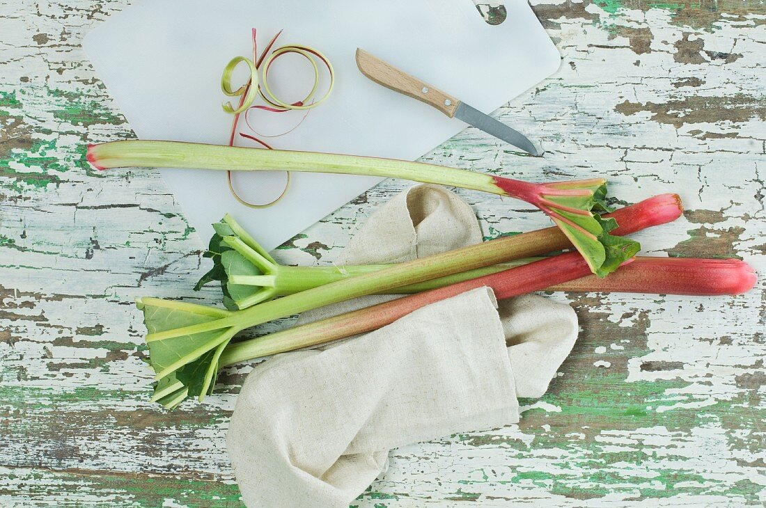 Sticks of rhubarb, a chopping board and a knife on a wooden table