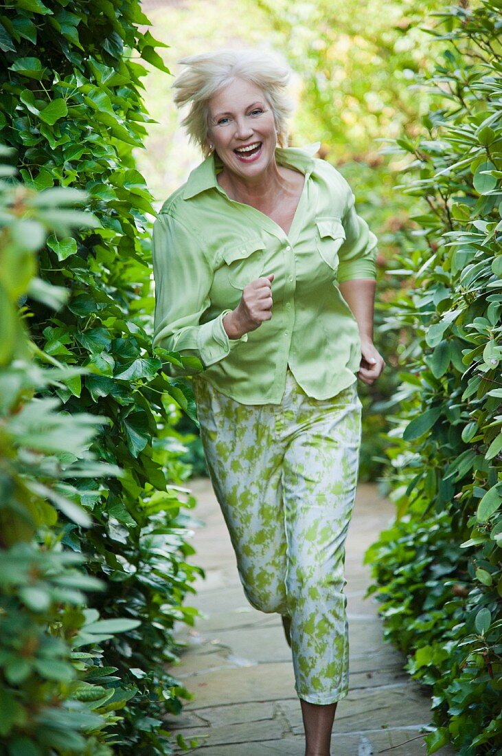 An older woman wearing a light green blouse and green-and-white trousers running in a garden