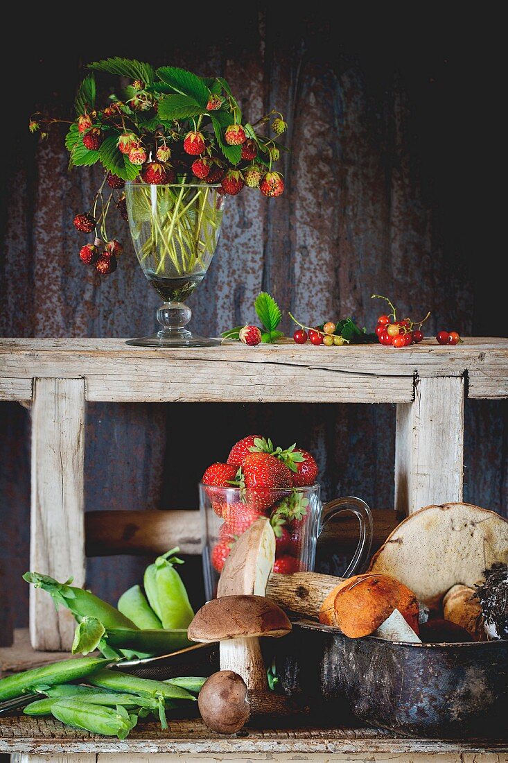 Wild mushrooms, young peas and strawberries on an old wooden table