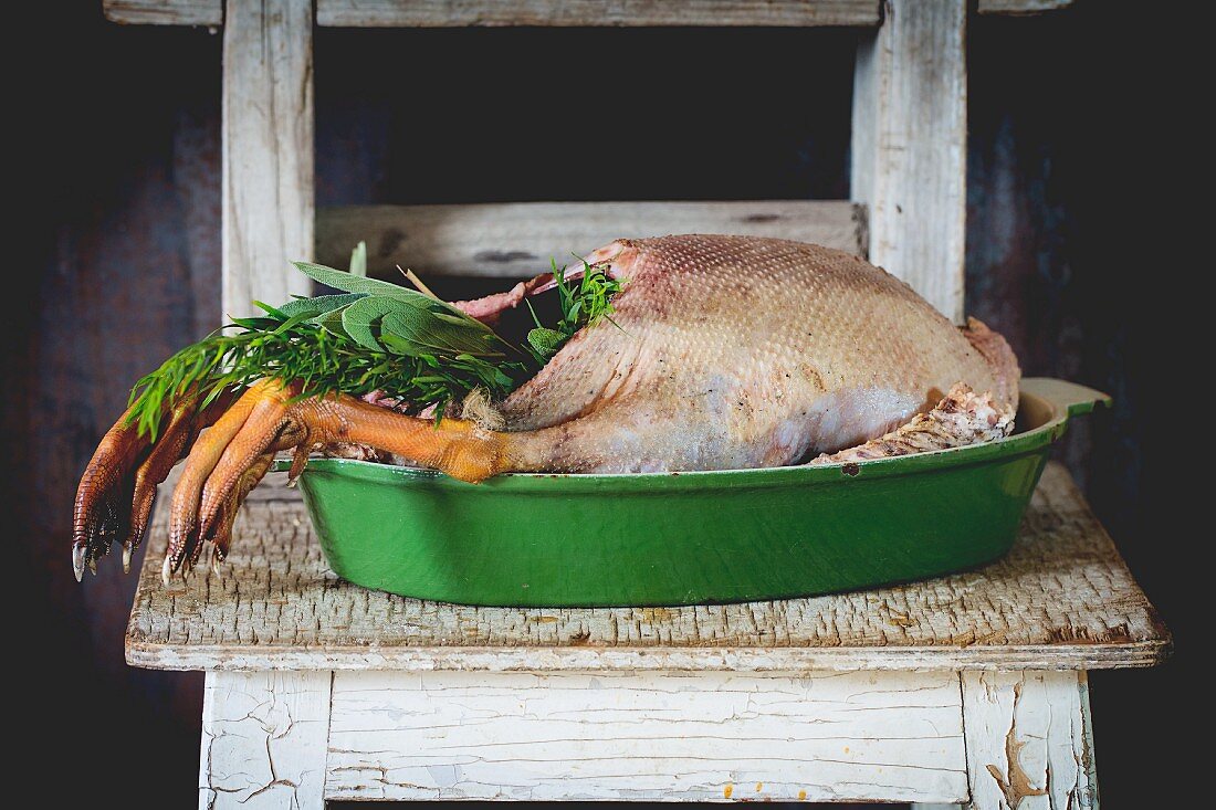 A ready-to-roast goose with a herb stuffing in a green roasting dish on a rustic wooden table