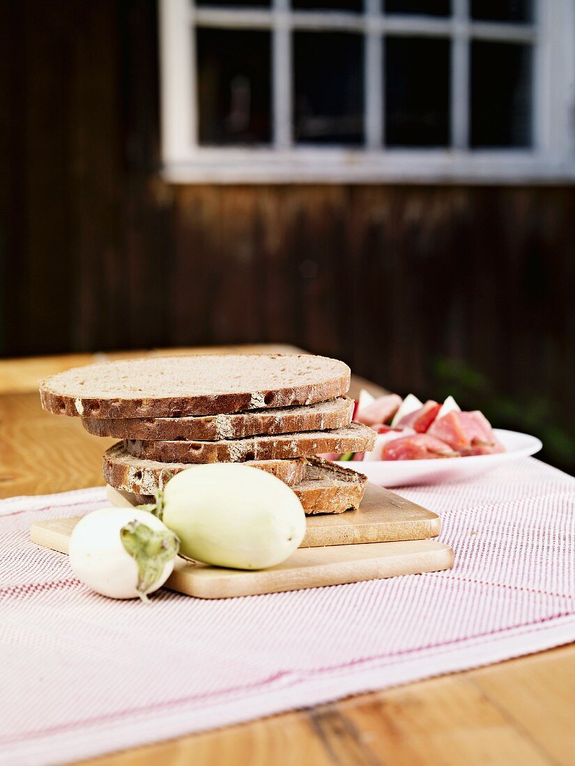 Sliced rye bread, white aubergines and raw ham on a table