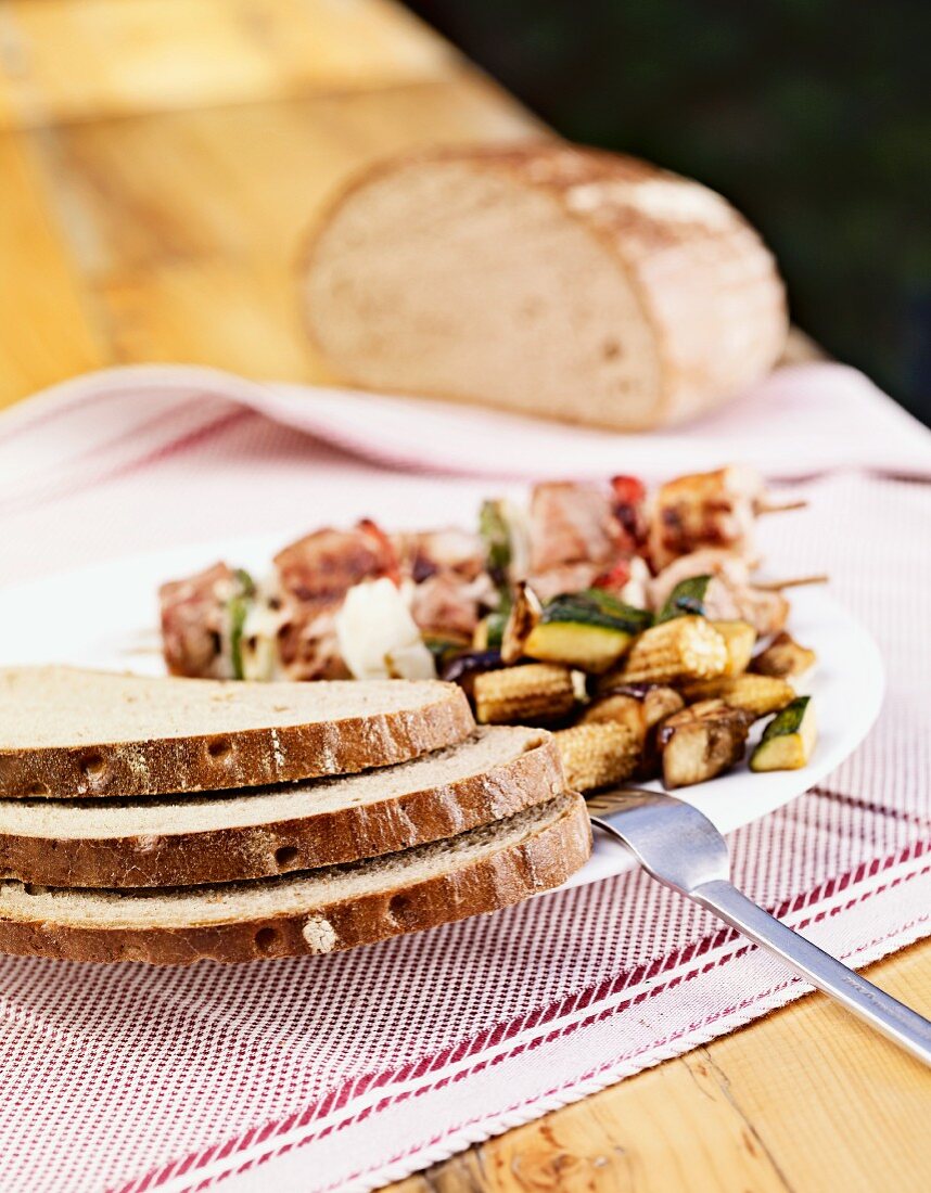 Slices of rye bread with vegetable salad and grilled skewers