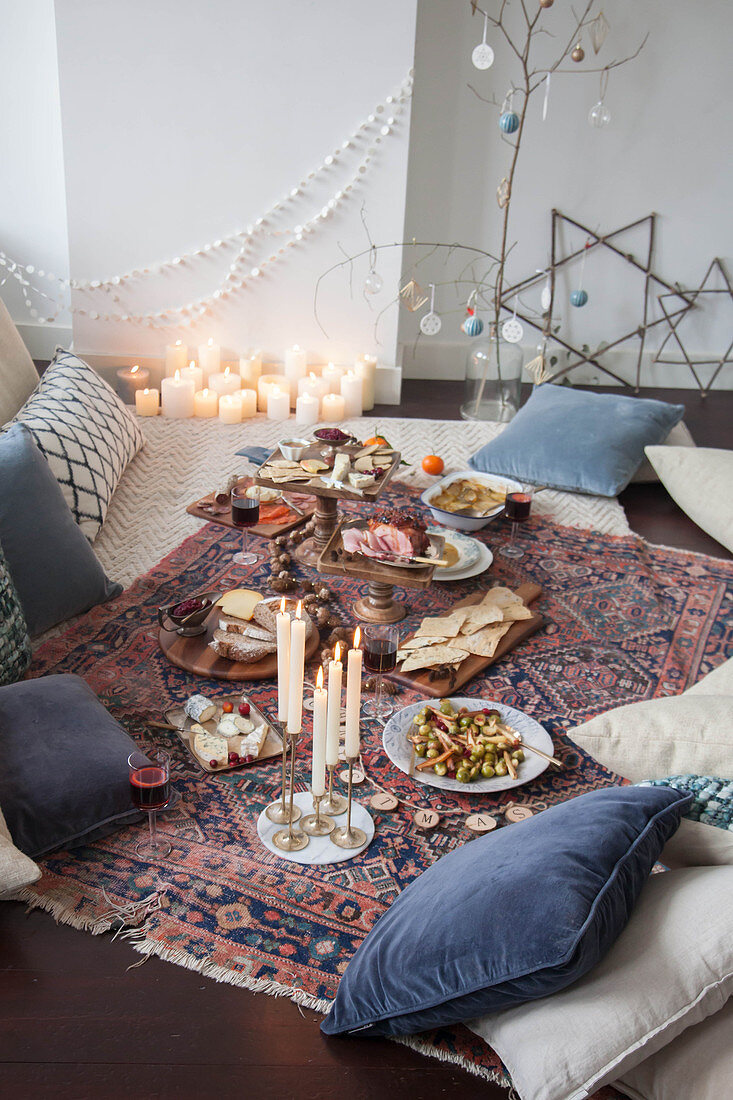 A picnic-style Christmas meal on a kilim rug with cushions and candles