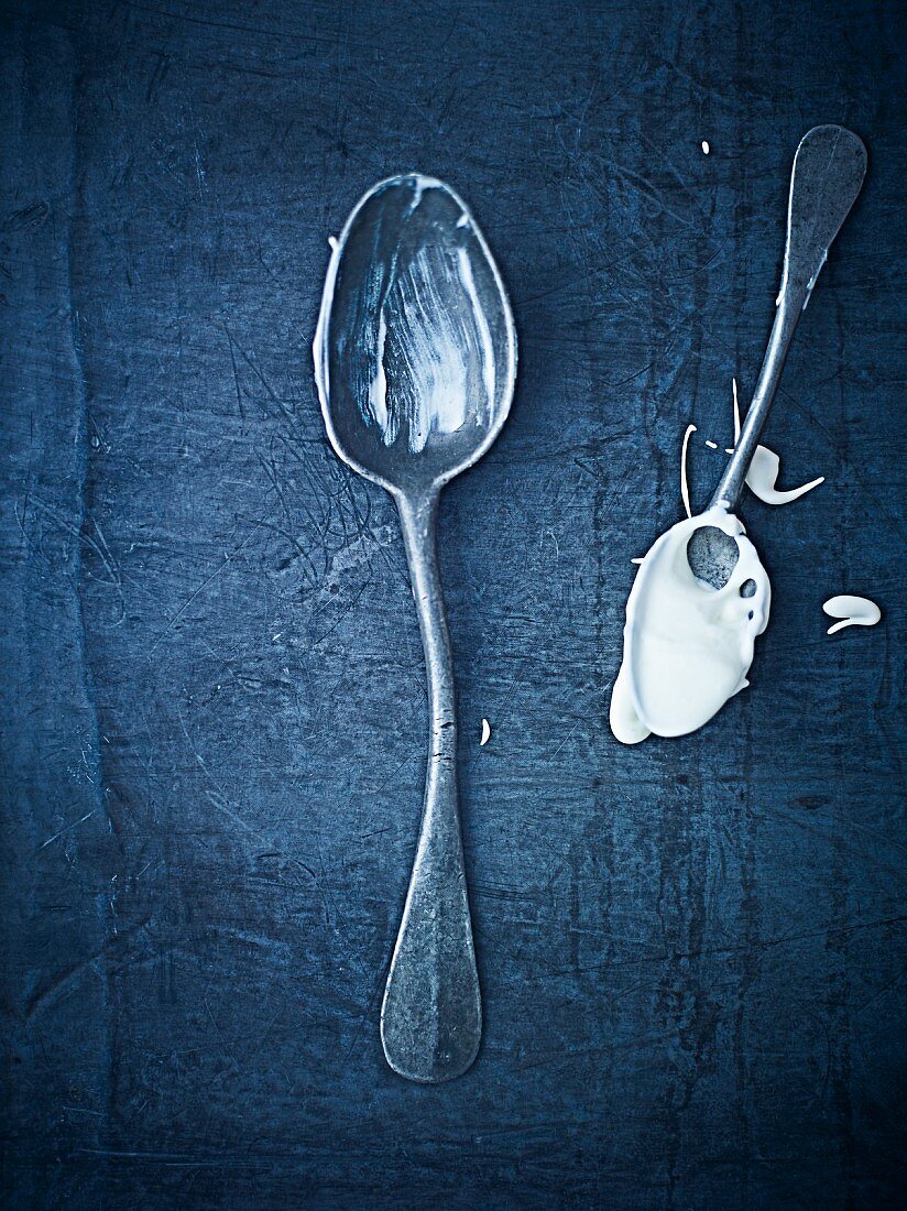 Two antique spoons with cream on them, one bent (seen from above)