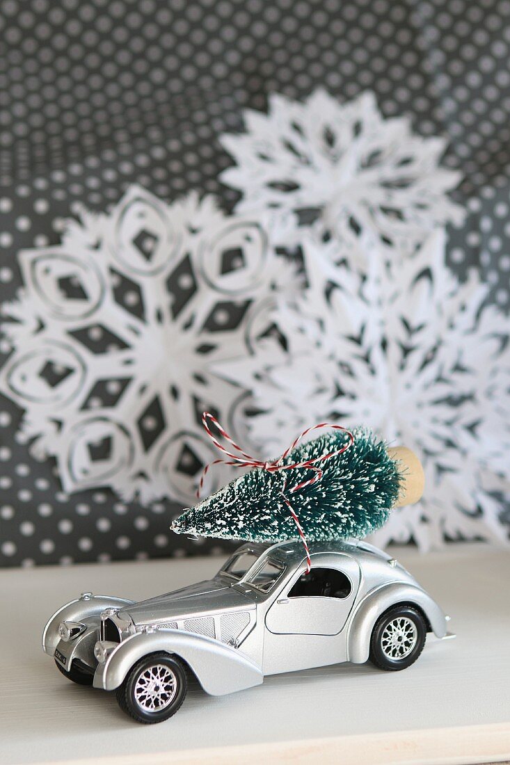 Toy car with Christmas tree on roof in front of paper snowflakes