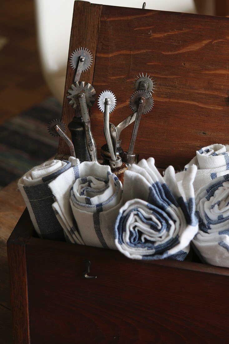 Rolled tea towels and vintage perforating tools in old wooden box with open lid