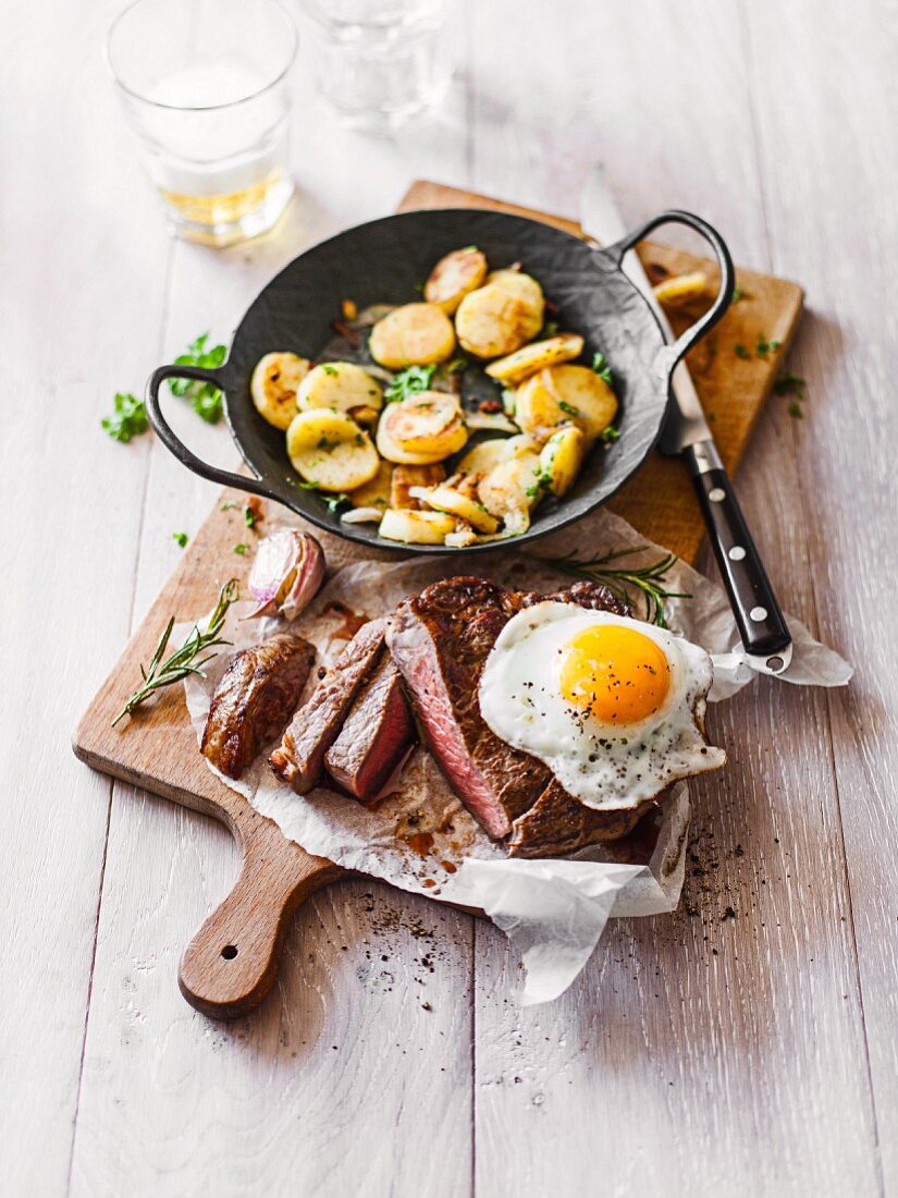 A rib-eye steak with a fried egg and fried potatoes