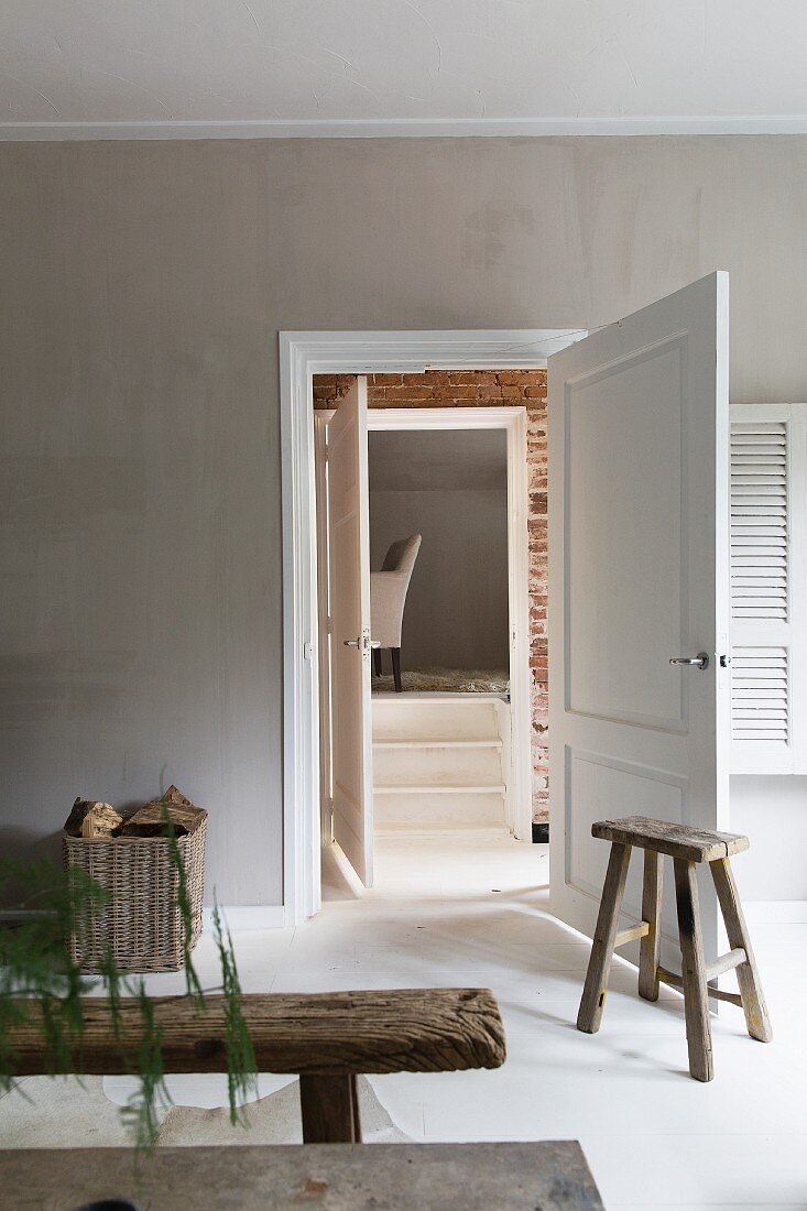 Wohnzimmer mit hellgrau getönter Wand, rustikale Holzbank und Holzhocker an der Tür