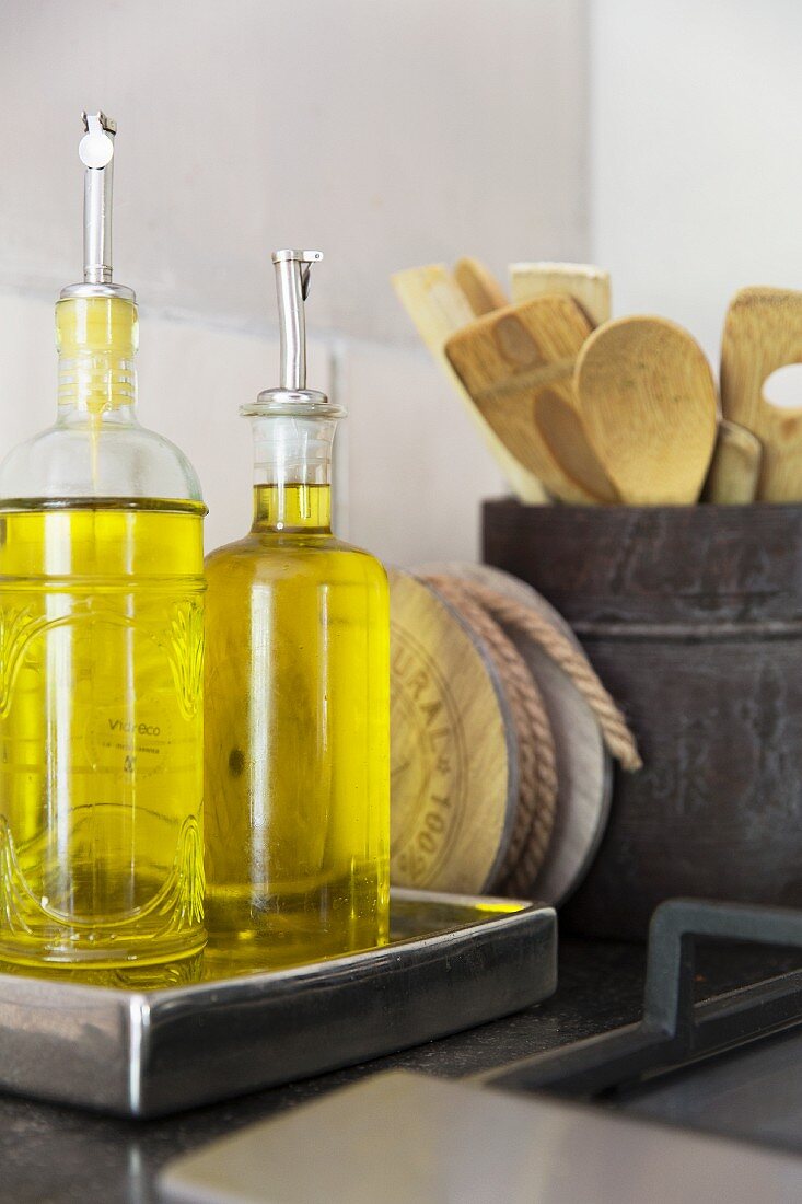 Bottles of oils with pouring spouts and pot of wooden spoons