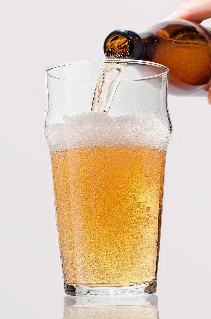 Helles Bier wird aus Flasche in Bierglas eingegossen