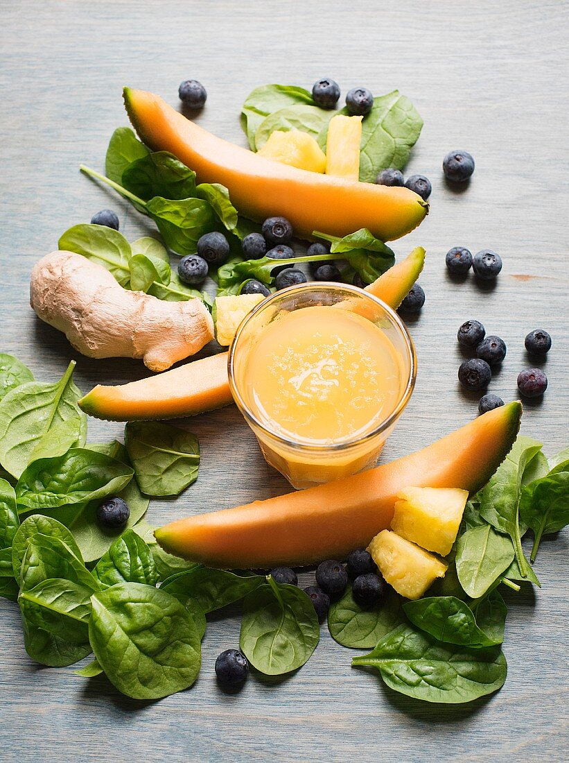 Melon and ginger smoothie surrounded by spinach leaves, blueberries and melon slices