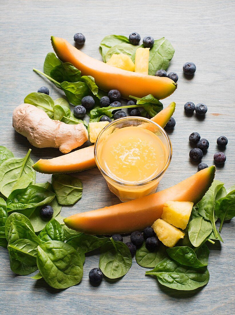 Melone-Ingwer-Smoothie im Glas zwischen Spinatblättern, Blaubeeren und Melonenscheiben