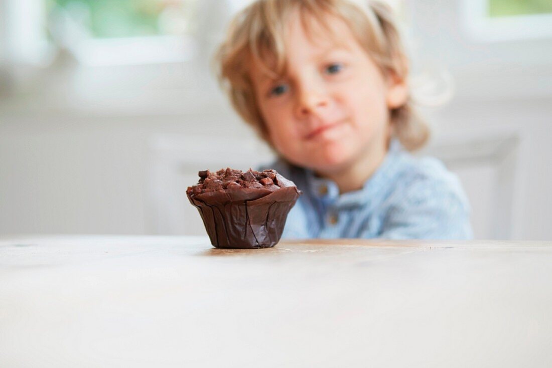 A little boy looking at a chocolate muffin