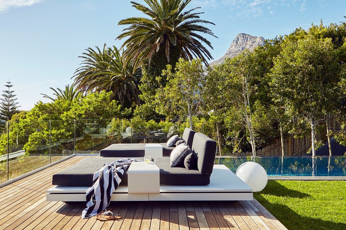 Modern loungers with cushions on terrace amongst palm trees