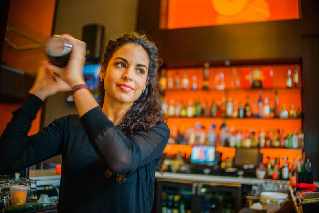 Junge Frau beim Schütteln eines Cocktailshakers in einer Cocktailbar
