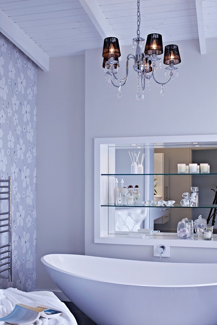 Chandelier above free-standing, designer bathtub; shelves in niche with mirrored wall