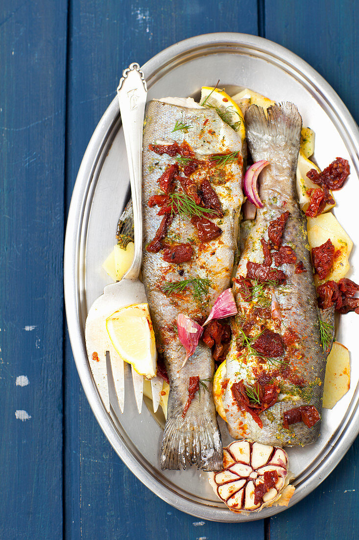 Baked trout with potatoes, lemons, garlic and dried tomatoes