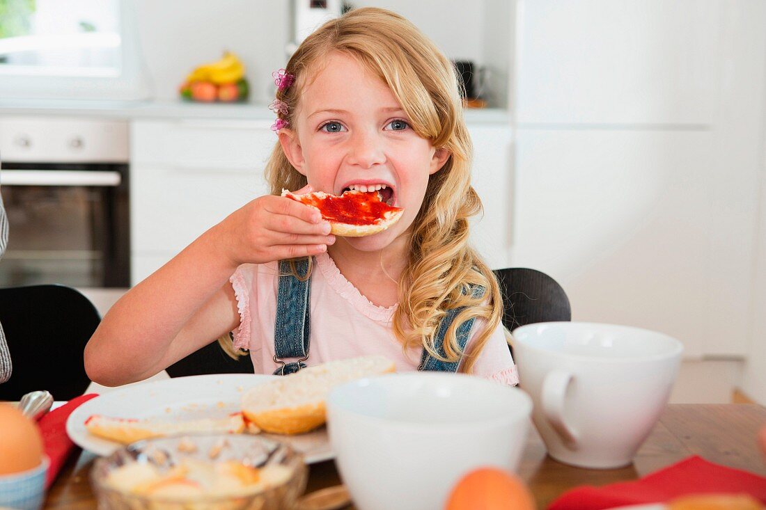Mädchen isst Marmeladenbrot am Küchentisch