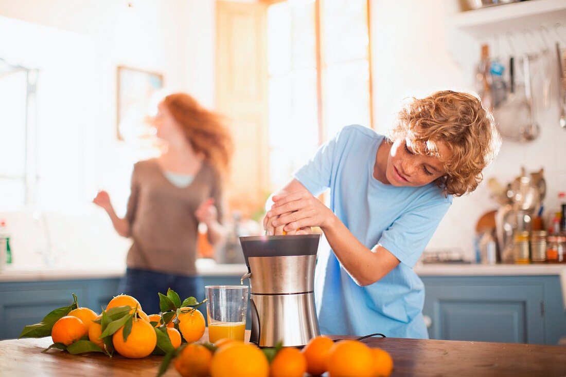 A teenage boy juicing oranges in a kitchen