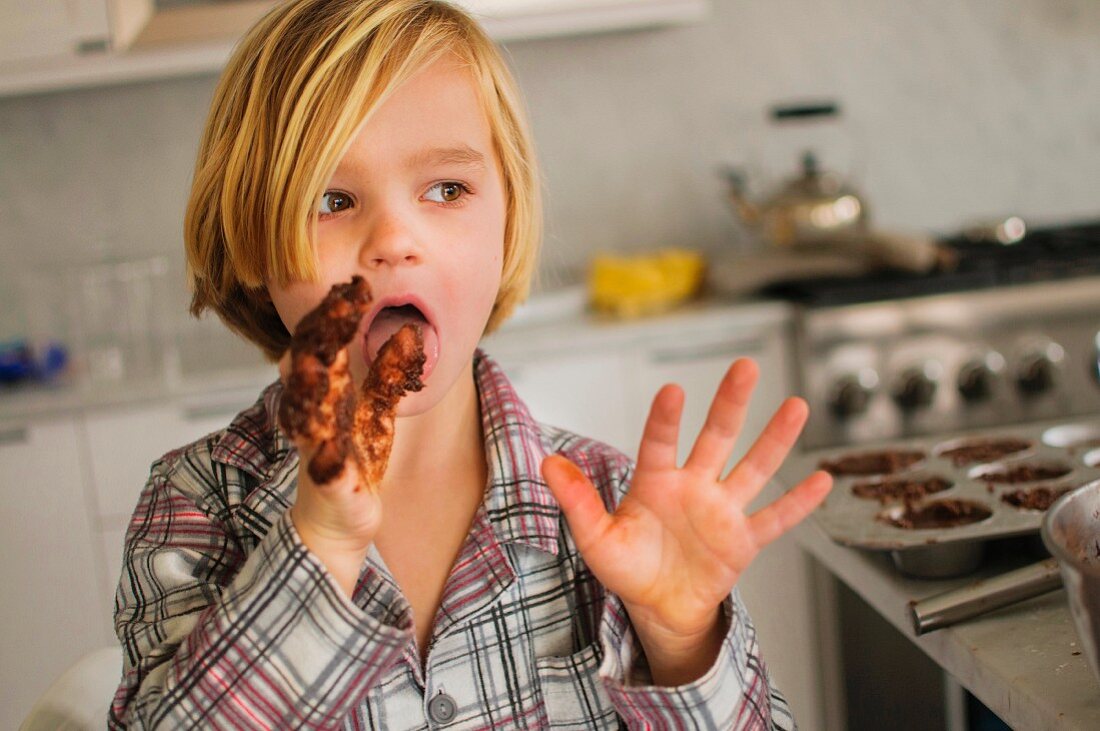 Junge schleckt Schokoladenteig von seinen Fingern
