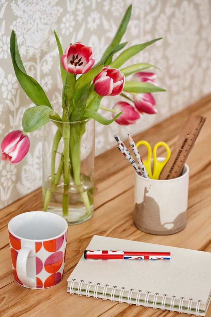 Tulpen und Becher auf Schreibtisch mit starker Holzmaserung vor hell gemusterter Tapete