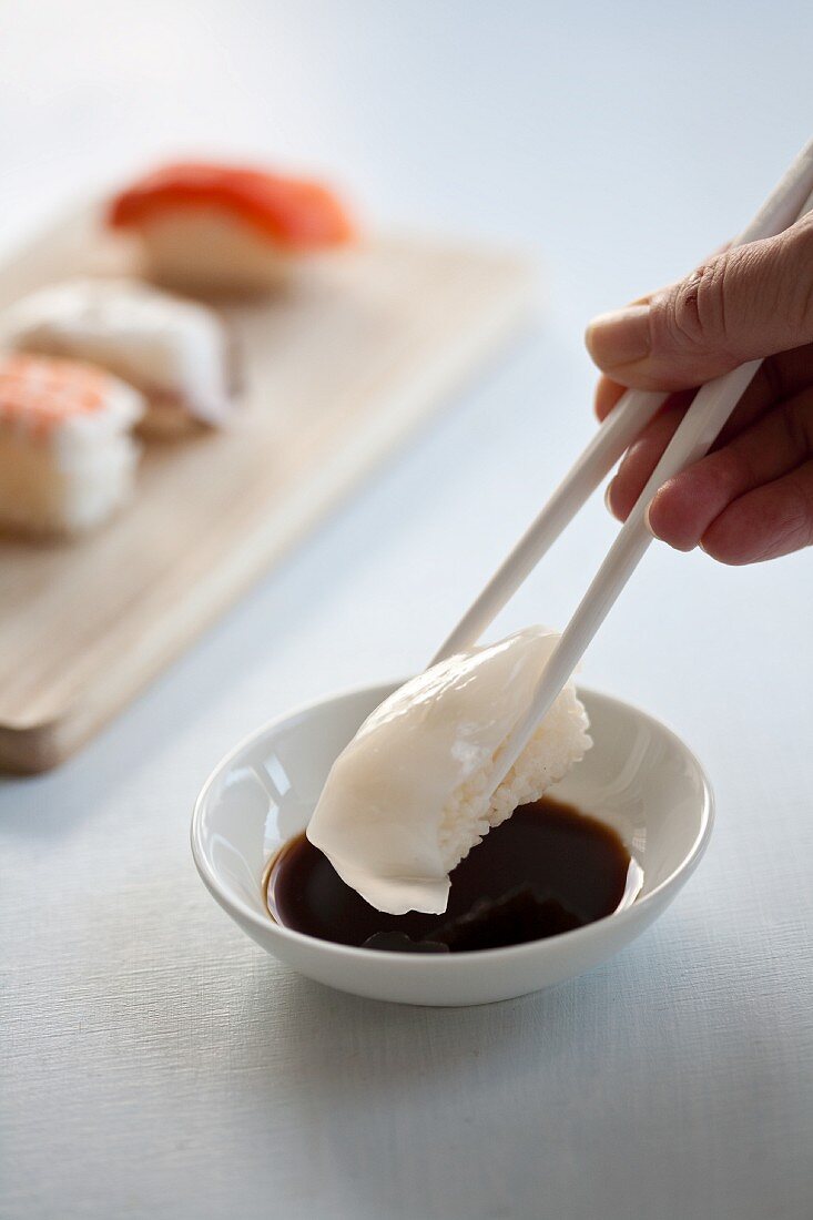 Nigiri sushi with squid being dipped in soy sauce