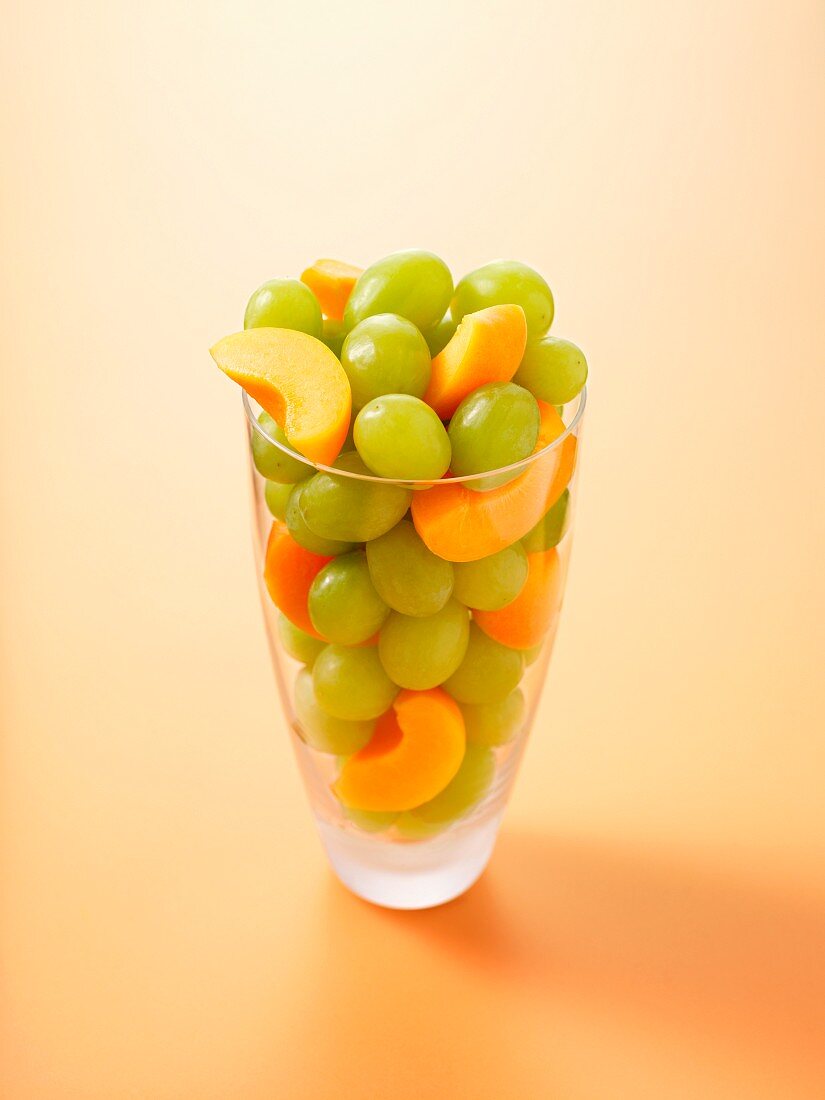 Trauben & Aprikosenspalten in Glas vor orangefarbenem Hintergrund