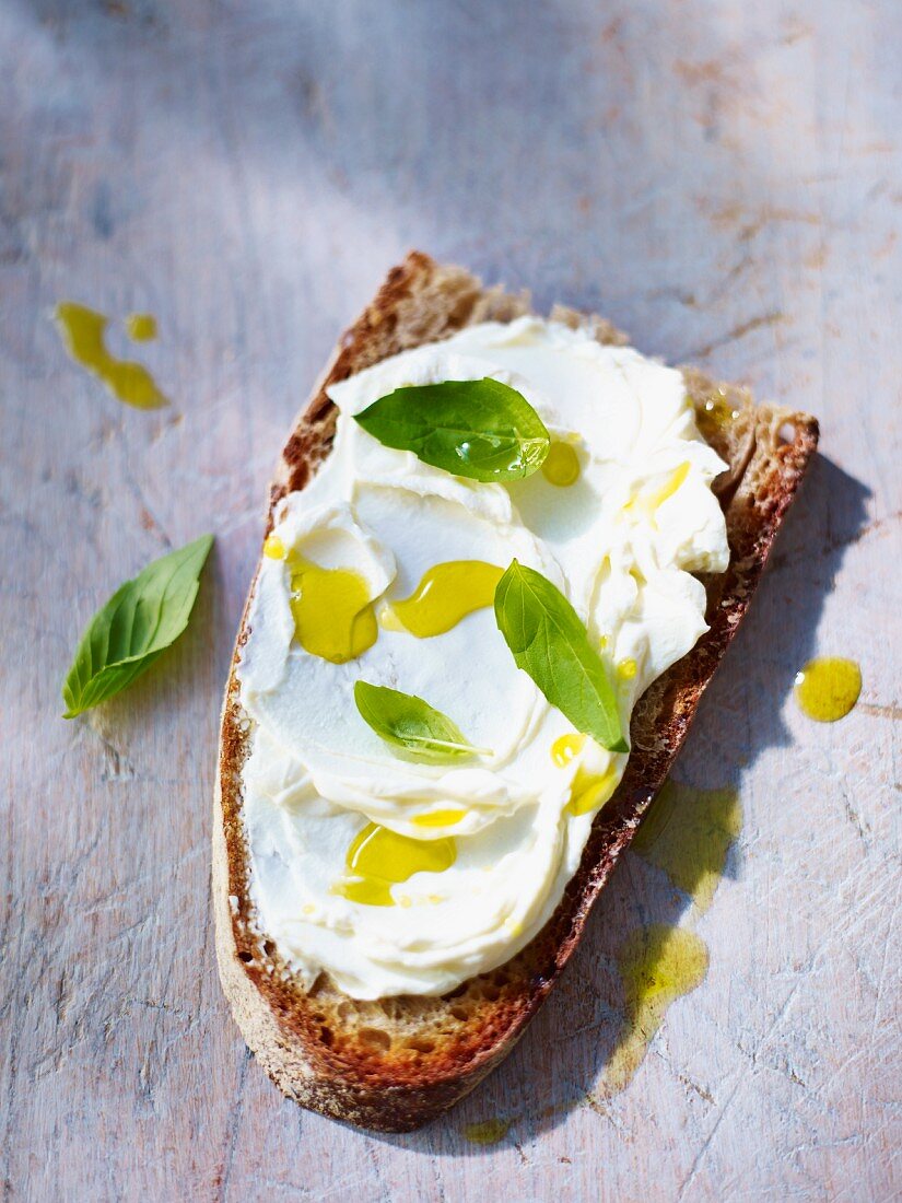 A slice of bread topped with cream cheese, olive oil and basil