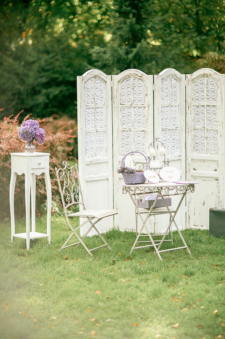 Garden table, ornate metal chair, vintage screen and vase of hydrangeas on side table