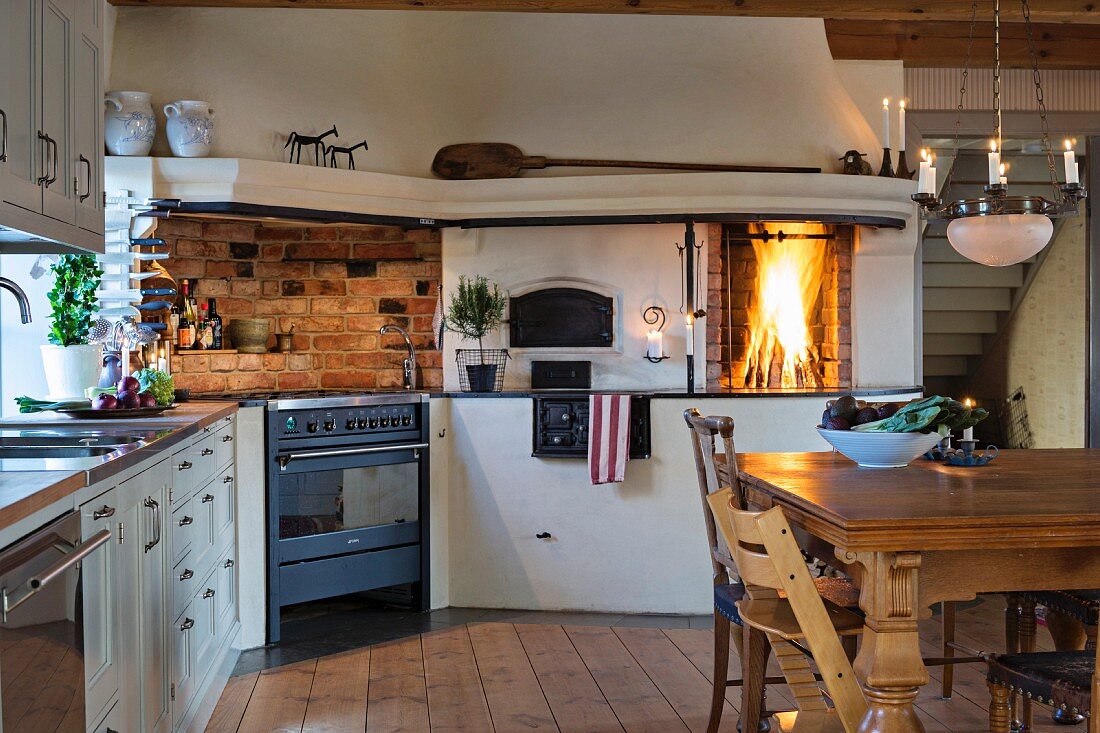 Landhaus-Essplatz mit Hänge-Kerzenleuchter in rustikaler Küche mit brennendem Kamin