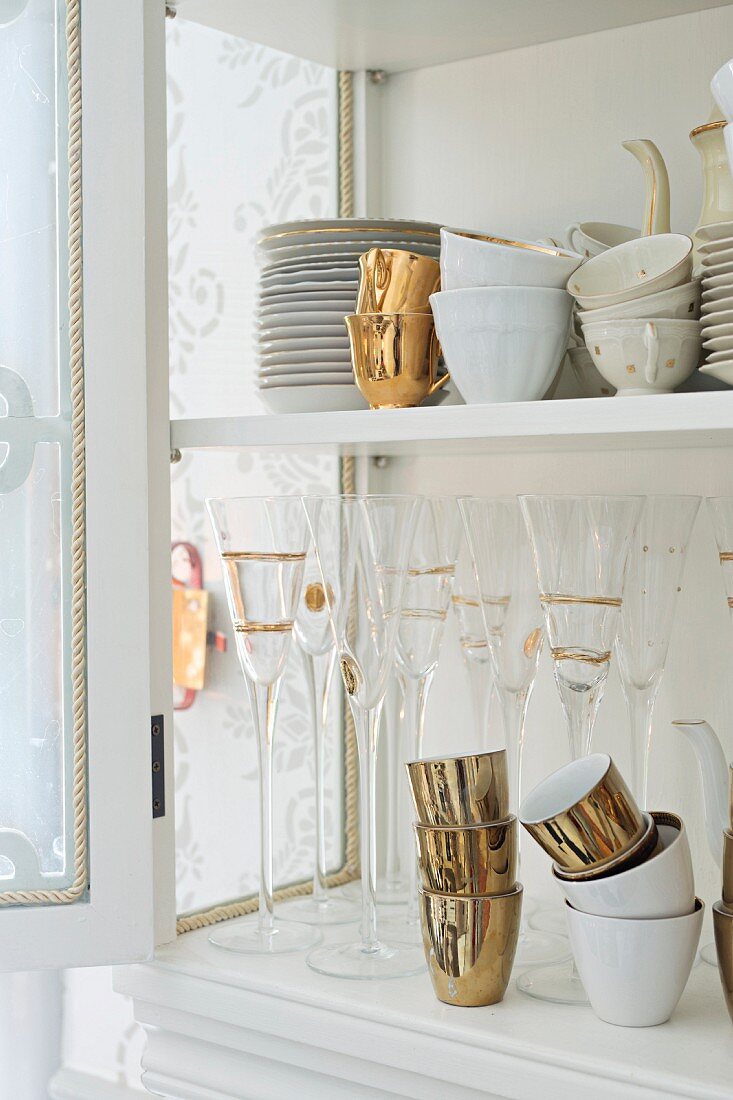 Plates, cups and glasses with gilt ornamentation in dresser