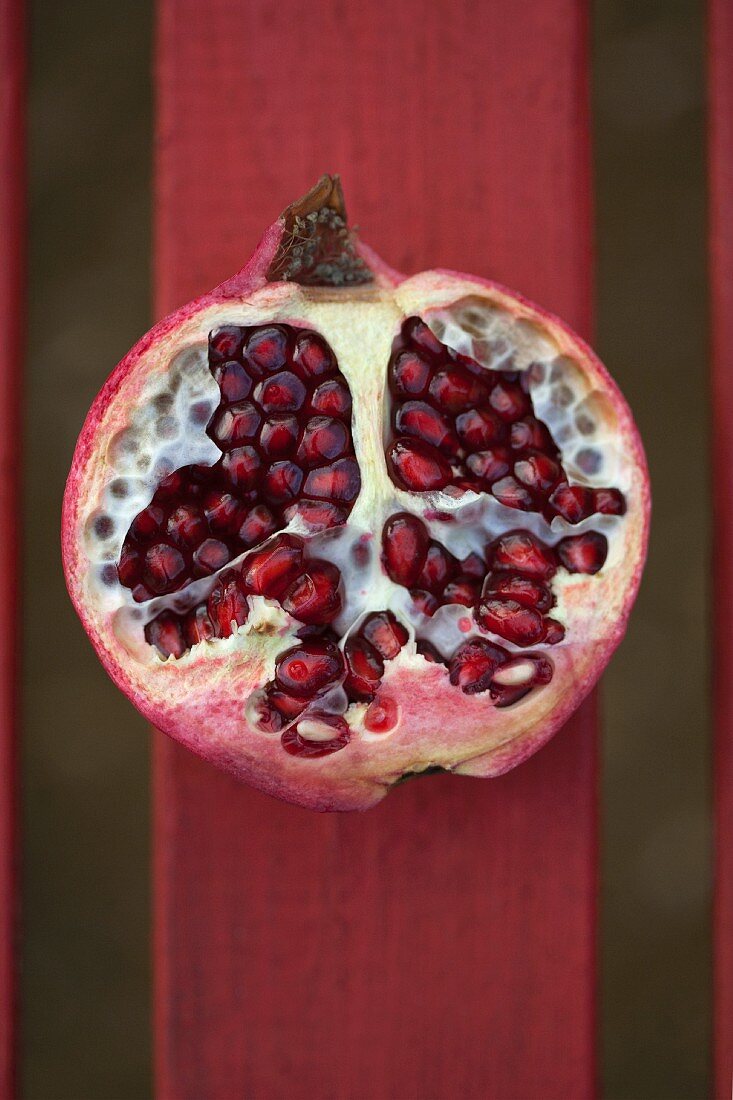 Ein halber Granatapfel auf roter Holzlatte (Aufsicht)