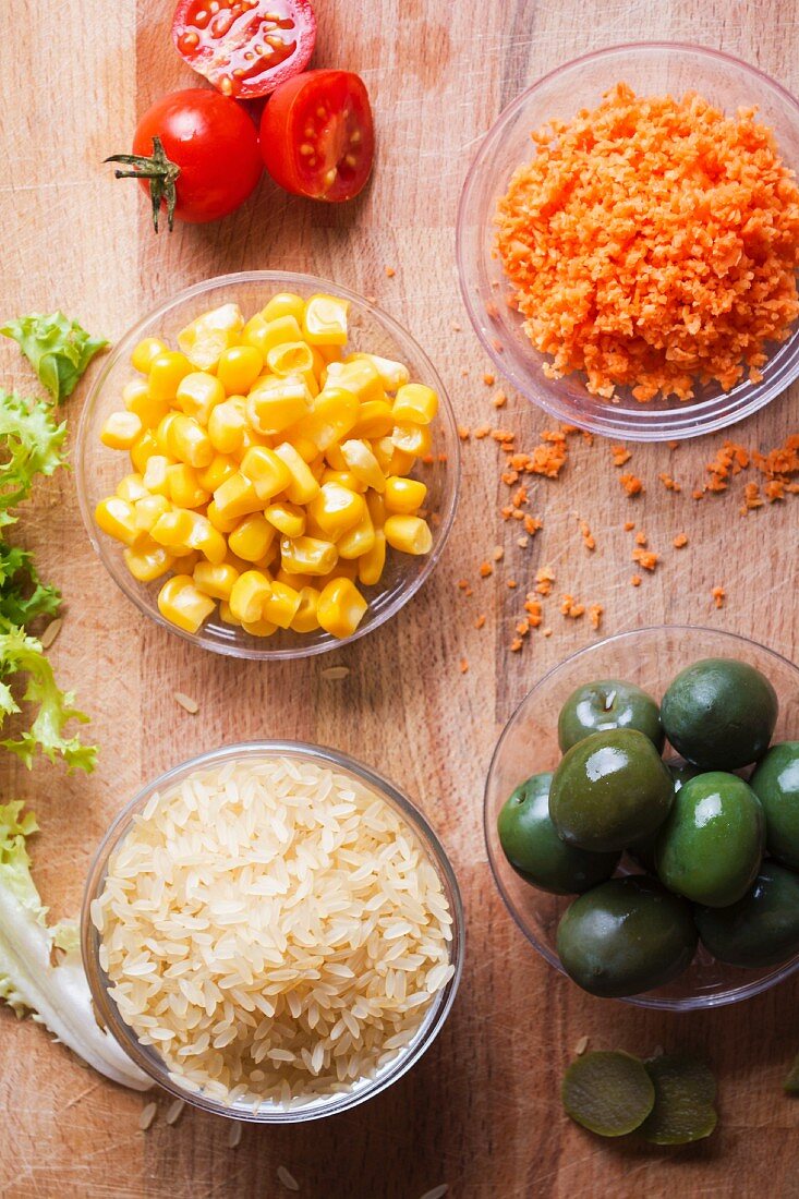 Ingredients for a rice salad with sweetcorn, green olives, tomatoes and carrots