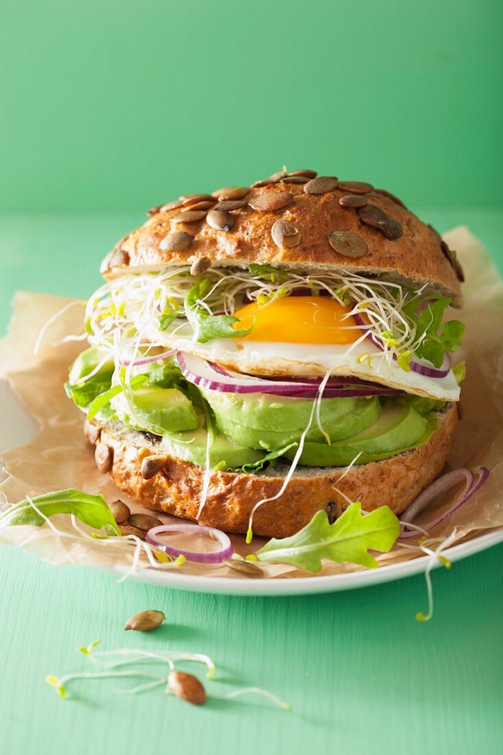 A sandwich with a fried egg, avocado and bean sprouts