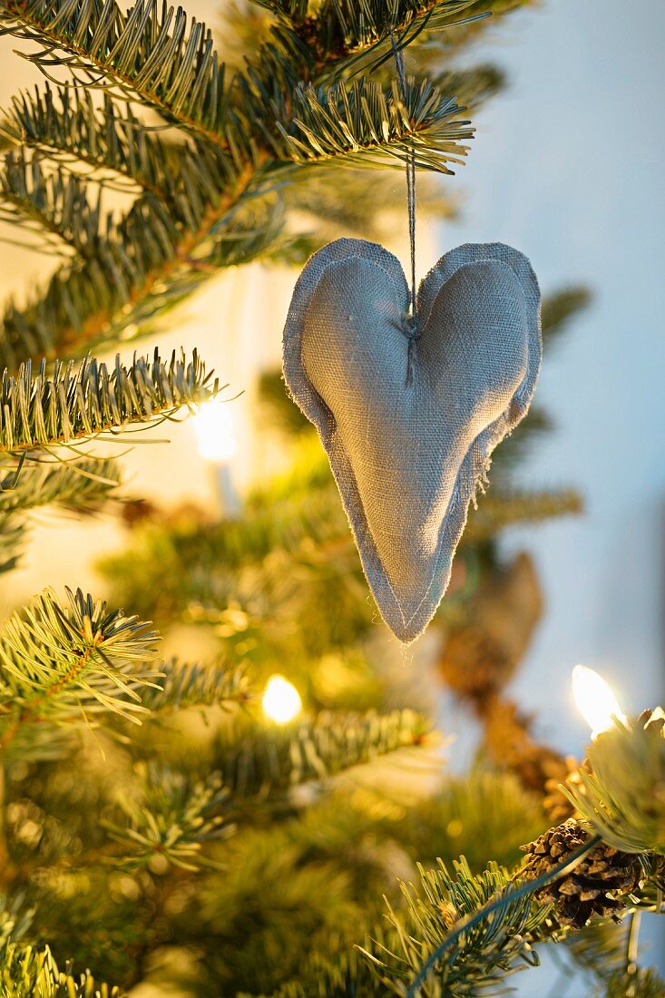 Ein Stoffherz aus Leinen als Anhänger im beleuchteten Weihnachtsbaum