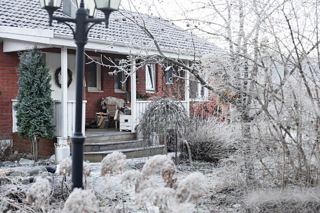 Backsteinhaus mit Veranda im winterlichen Garten mit Raureif