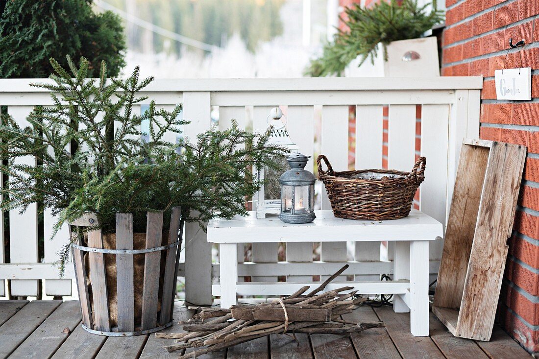 Tannenbaum im Holzkorb neben Bank mit Laternen auf der Veranda