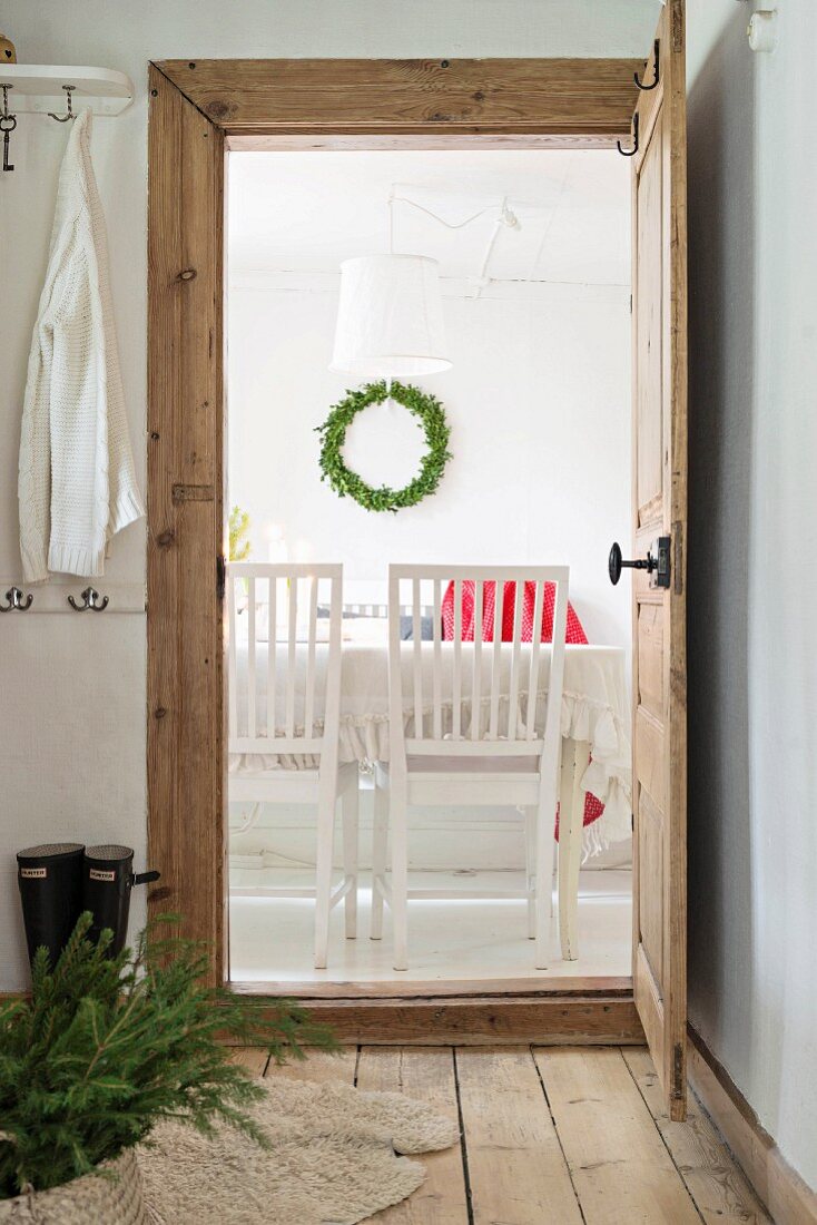 Basket of fir branches on wooden foyer floor and view of wreath on dining room wall through open door